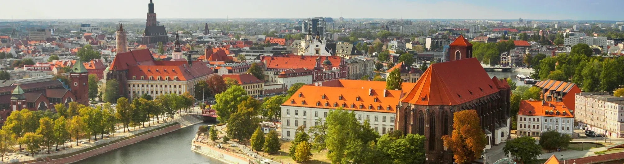 Panoramic aerial view of Wroclaw cityscape with the Odra River, historic buildings with red roofs, church towers, and lush gr