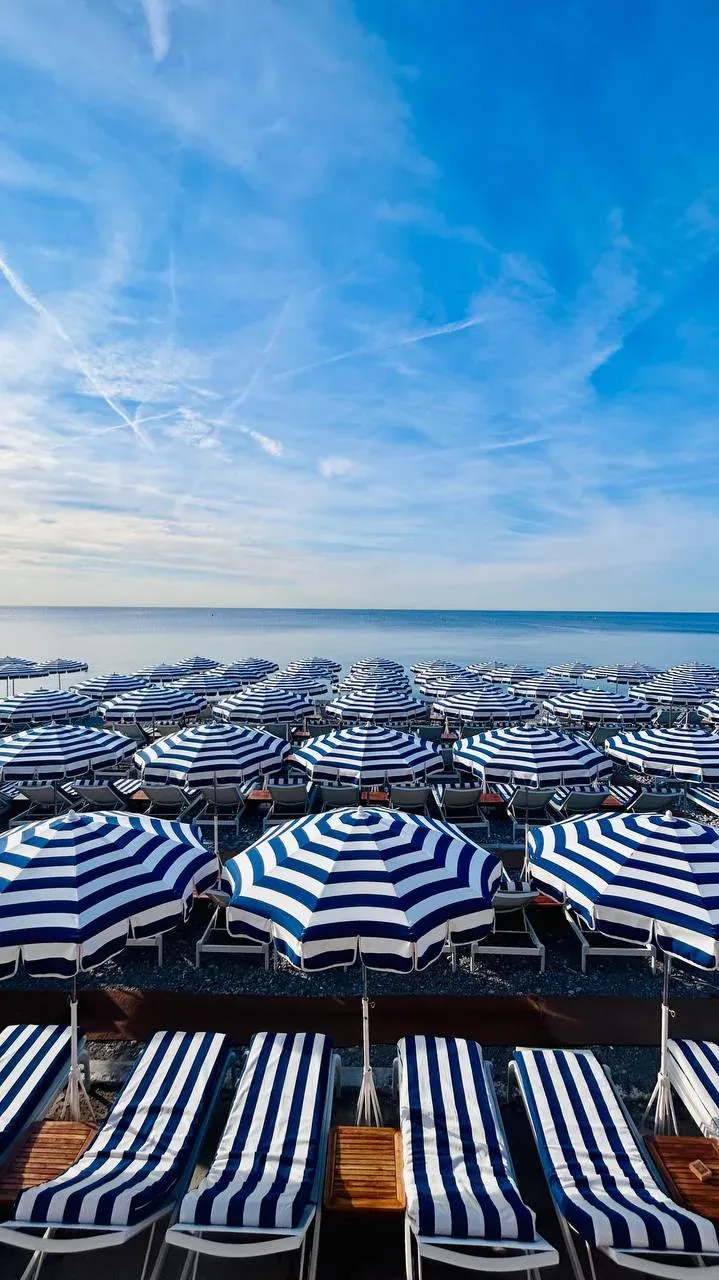 Reihen von blau-weiß gestreiften Sonnenschirmen und Liegestühlen an einem Strand in Nizza.