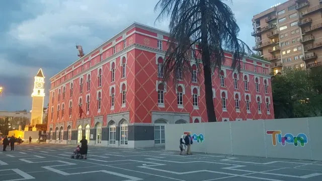 Turistas explorando un vibrante edificio rosa y una torre del reloj en Tirana, Albania.