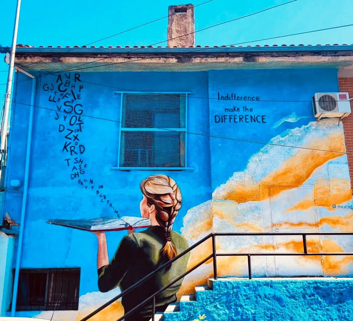 Colorful street art mural of a woman holding a book on a blue building.