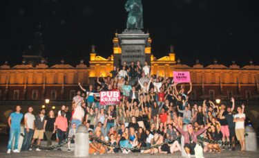 a lot of people having fun on pub crawl next to statue of Adam Mickiewicz in Krakow