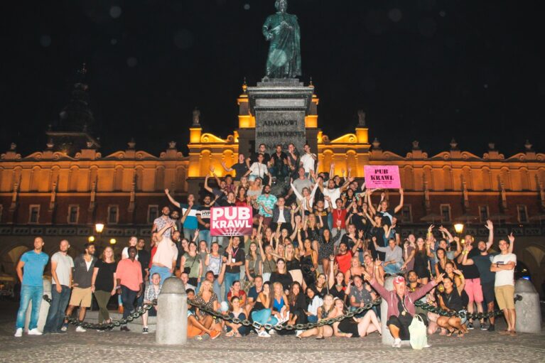 a lot of people having fun on pub crawl next to statue of Adam Mickiewicz in Krakow